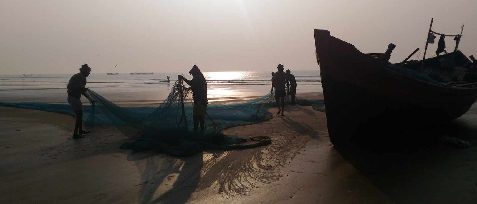 Silhouette image of people by the beach with fishing net and boat