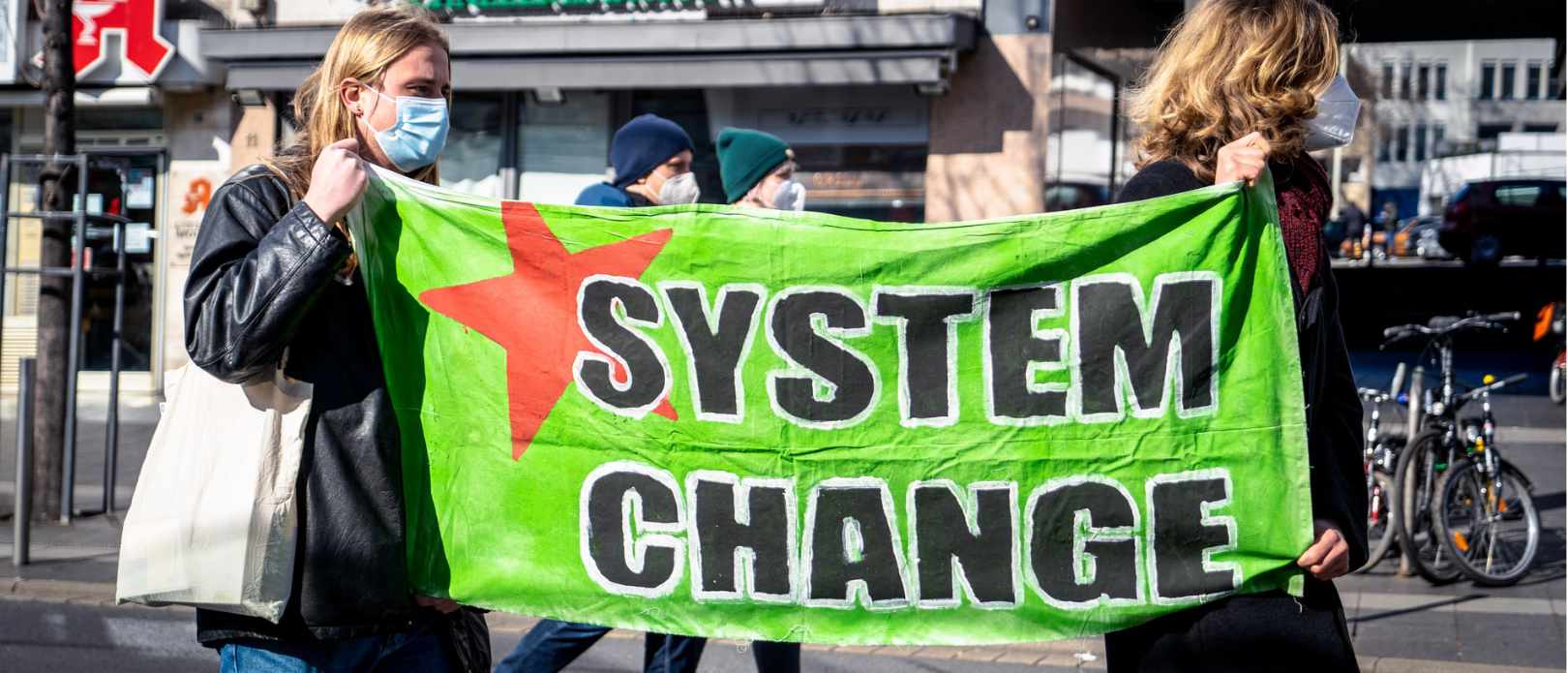 Two women holding a sign saying "System change"